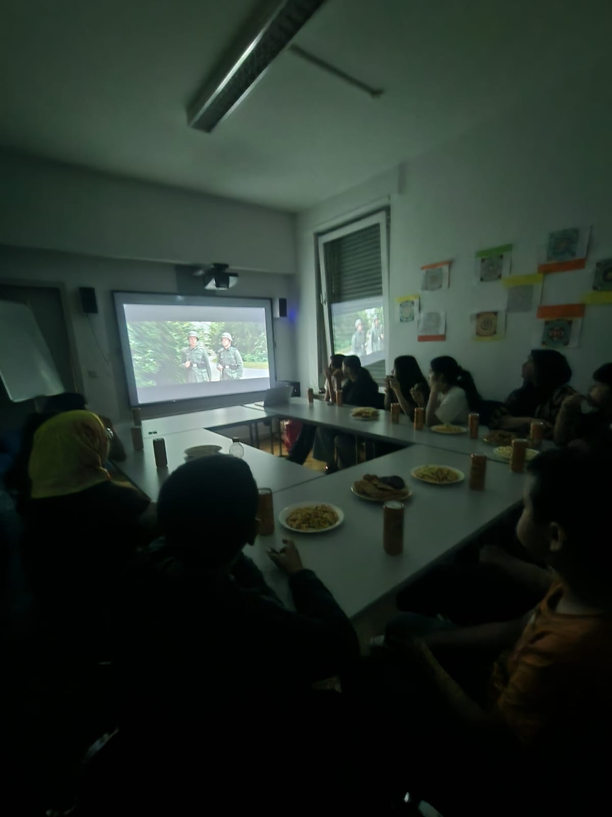 Jugendliche in einem abgedunkelten Raum schauen gemeinsam einen Film auf einer Leinwand an.